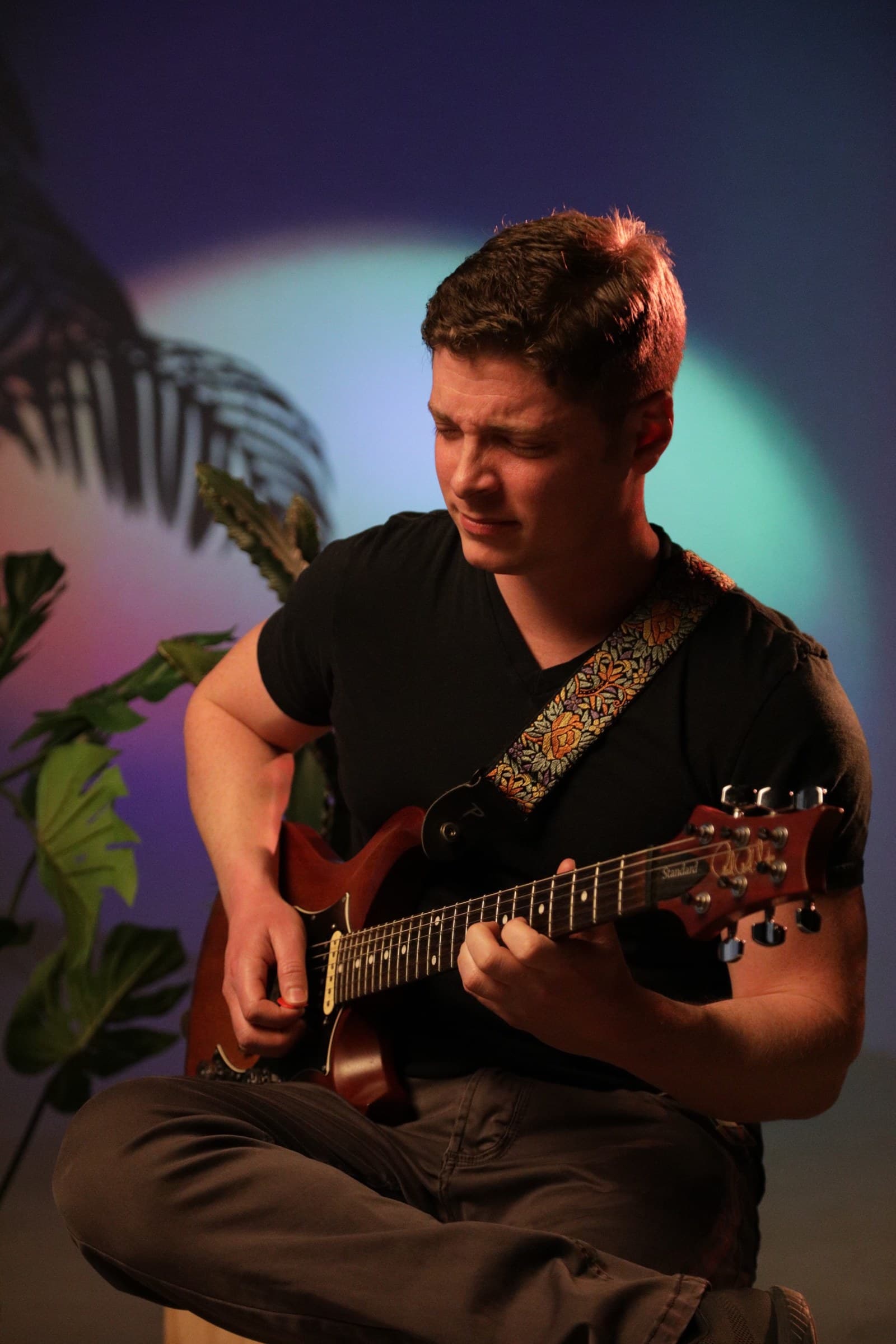 Julian Goddard playing his electric guitar under warm studio light, eyes closed, mid-phrase